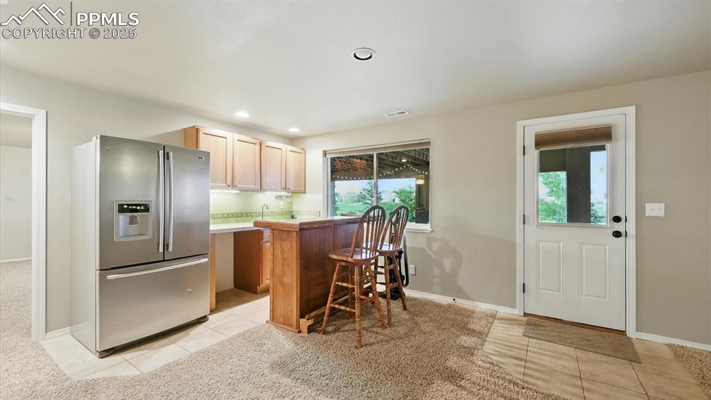 Image 13 of 50: Basement wet bar with French door refrigerator and walk out to the covered 