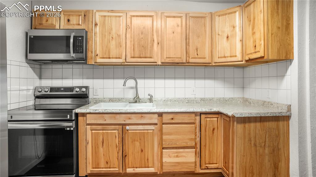 Image 10 of 20: Kitchen featuring stainless steel appliances, backsplash, light countertops