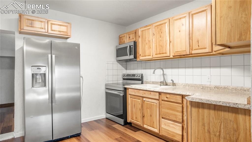 Image 9 of 20: Kitchen featuring backsplash, stainless steel appliances, light wood finish