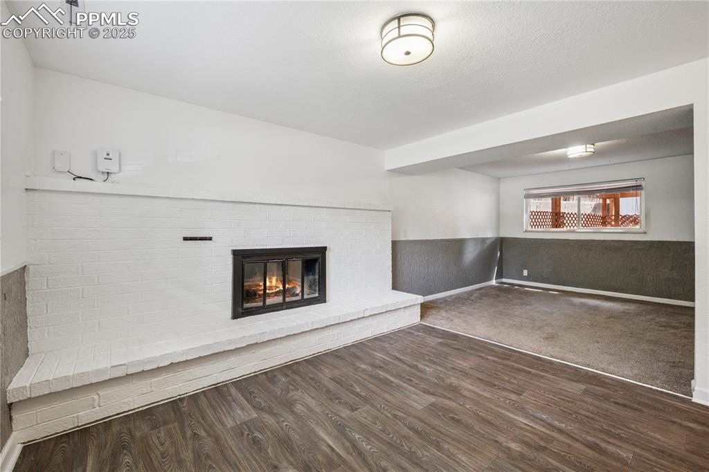 Image 29 of 35: Family room with a wainscoted wall, a brick fireplace, dark wood-style floo