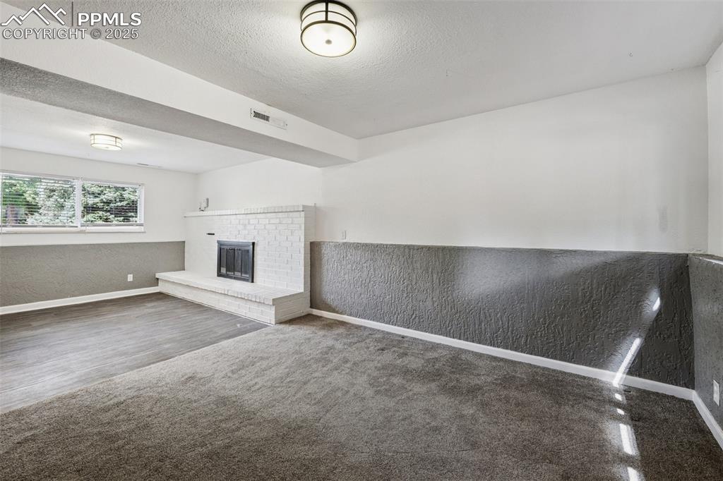 Image 31 of 35: Unfurnished family room featuring a textured ceiling, a fireplace, wainscot