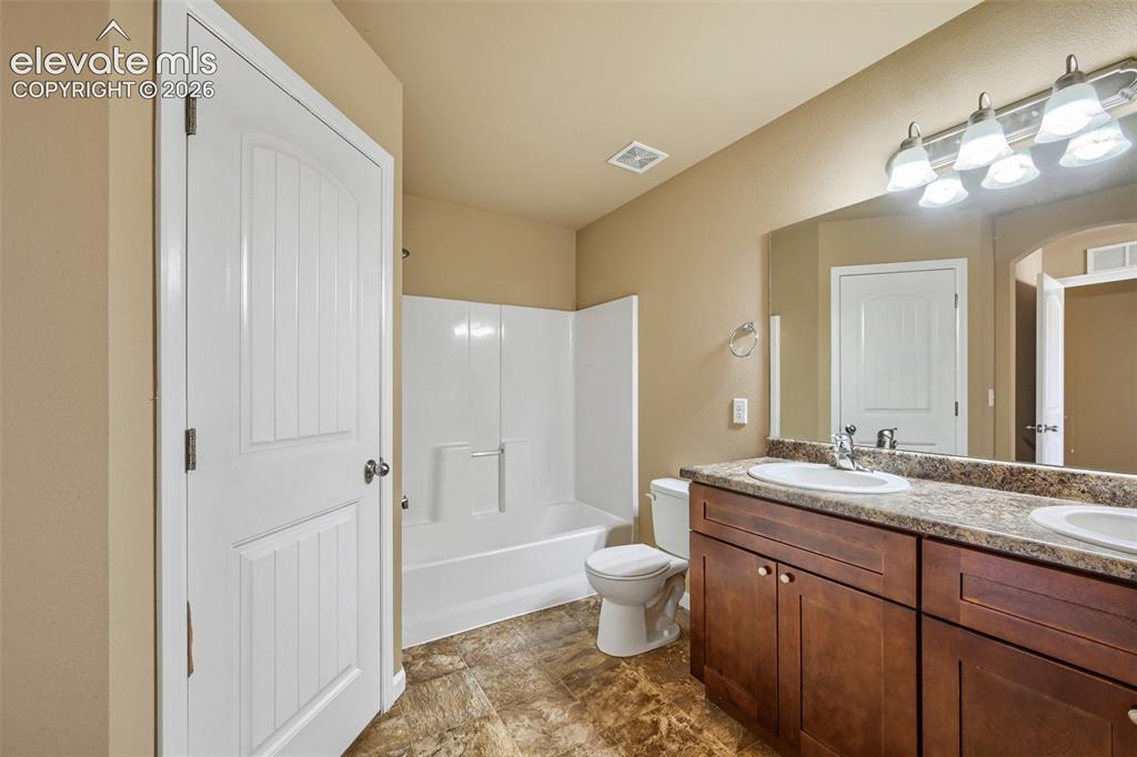 Image 13 of 25: Bathroom featuring a double vanity with wood-finish cabinetry and integrate