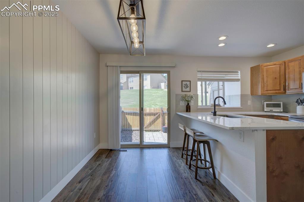 Image 12 of 30: Kitchen with a breakfast bar area, dark wood-style flooring, light stone co