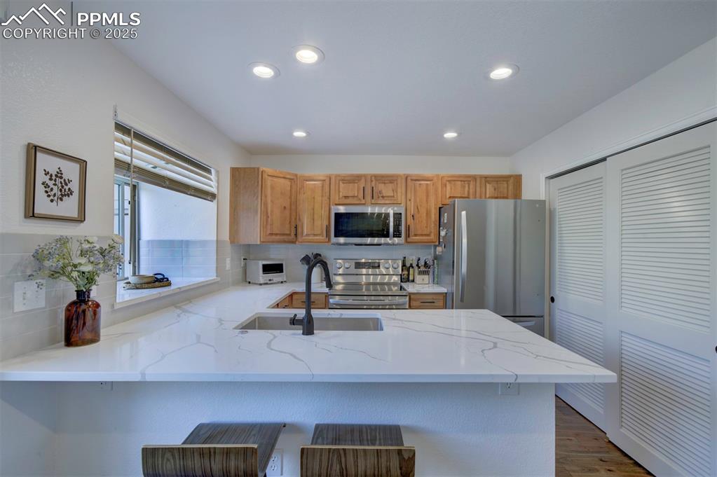 Image 8 of 30: Kitchen with a peninsula, stainless steel appliances, light stone counters,