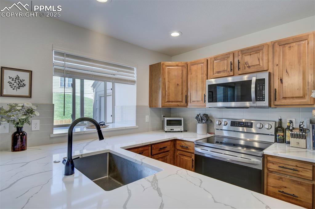 Image 9 of 30: Kitchen featuring appliances with stainless steel finishes, brown cabinetry