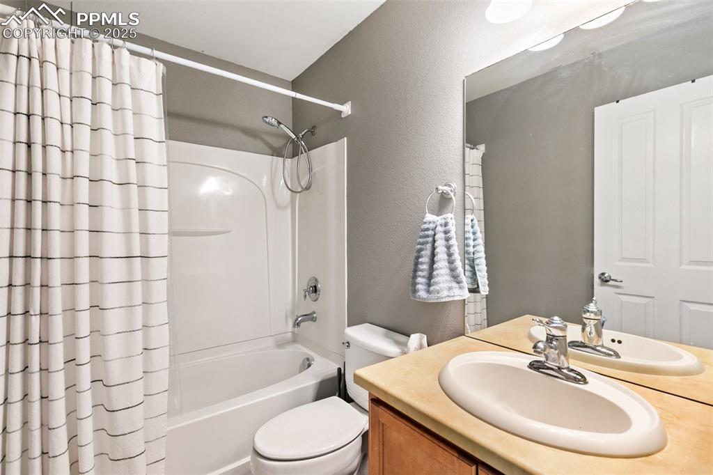 Image 21 of 36: Bathroom with toilet, vanity, a textured wall, and shower / tub combo