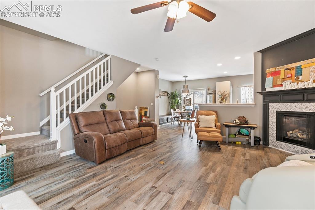 Image 6 of 36: Living room with stairs, wood finished floors, a ceiling fan, a tile firepl