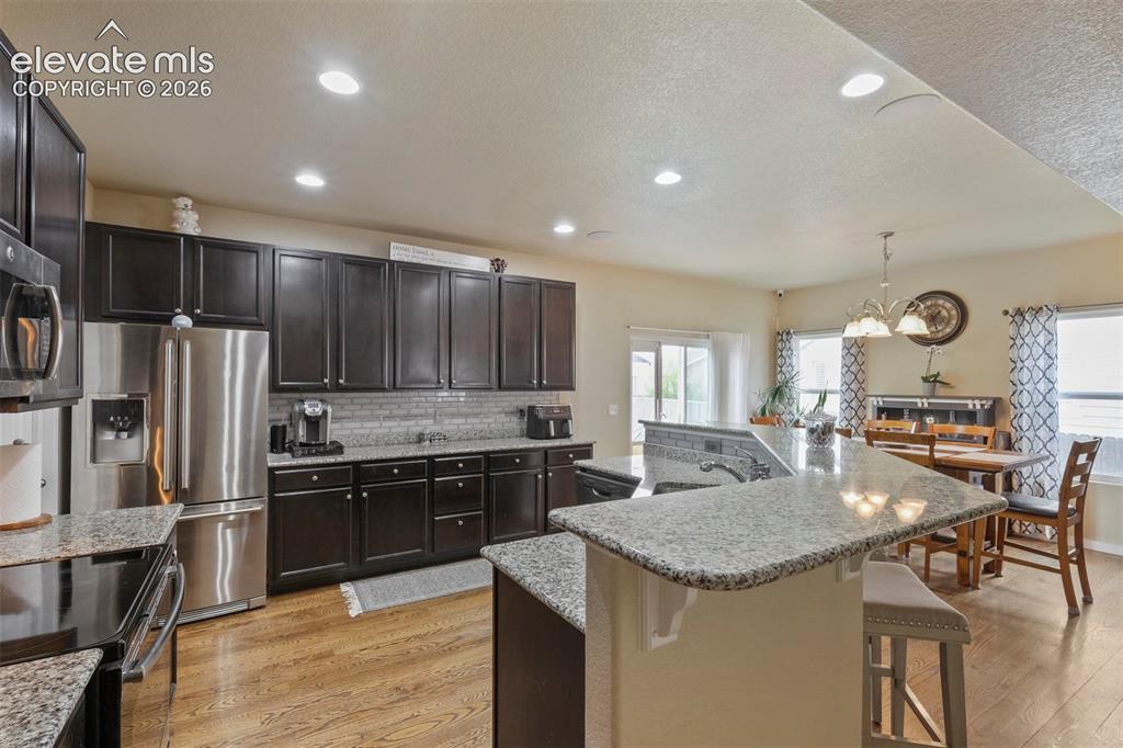 Image 10 of 33: Kitchen featuring wood-finish flooring, dark wood cabinetry, and light-tone