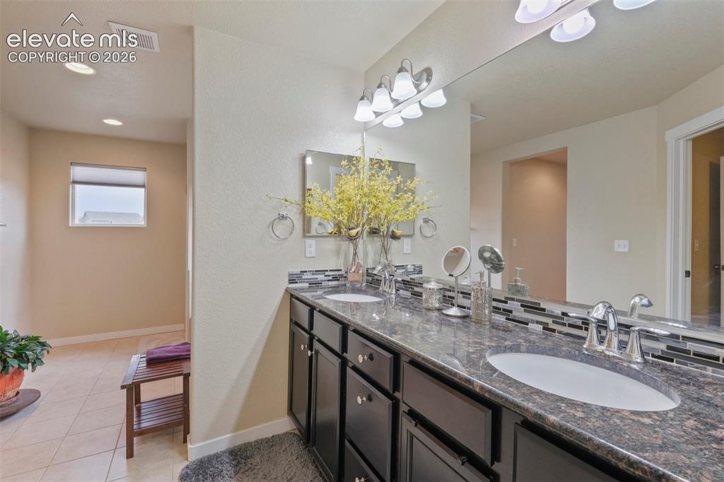 Image 15 of 33: Upper Level: Dual vanity featuring dark cabinetry, stone countertop, and tw