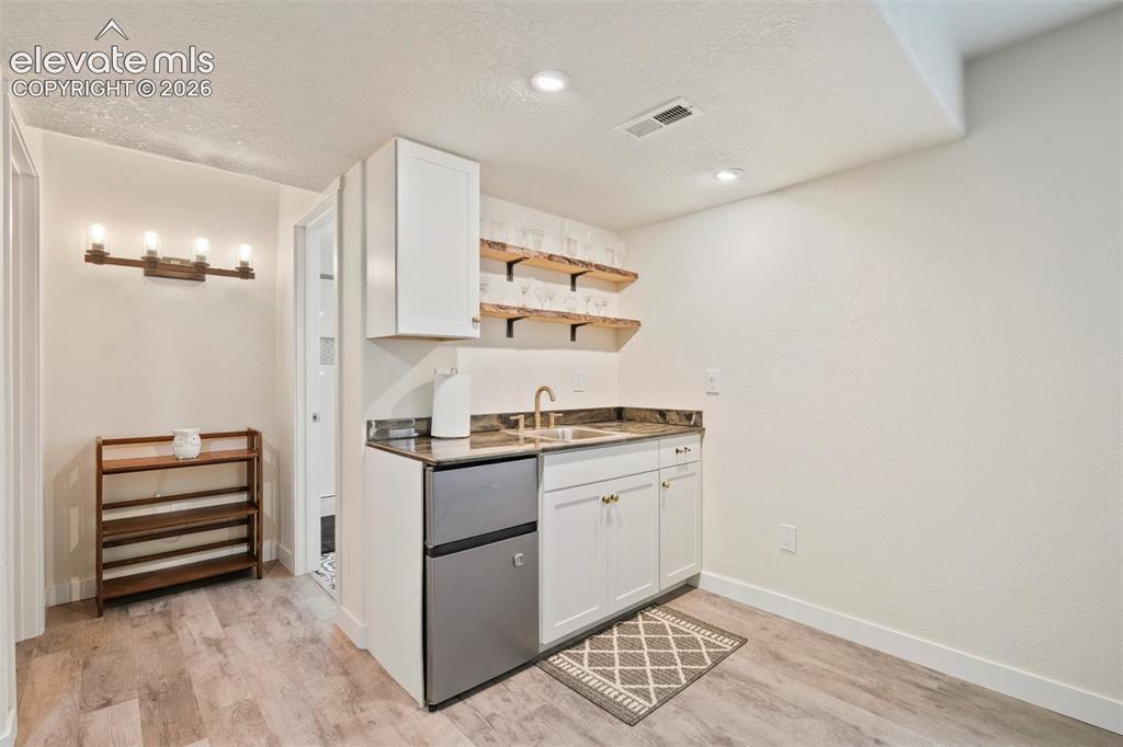 Image 25 of 33: Basement: Wet bar featuring a compact refrigerator, single basin sink with 