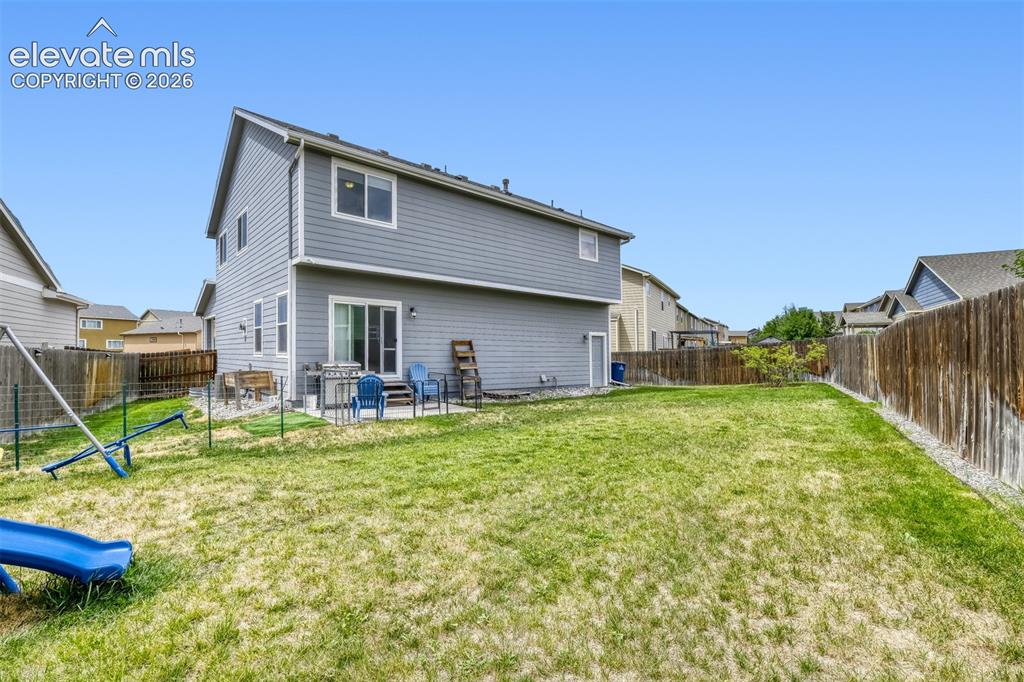 Image 29 of 33: Expansive green lawn with a two-story residence featuring grey siding