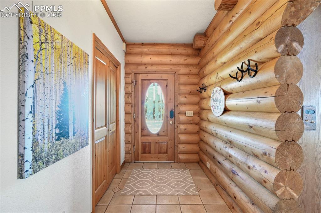 Image 11 of 50: Doorway to outside featuring light tile patterned floors and rustic walls