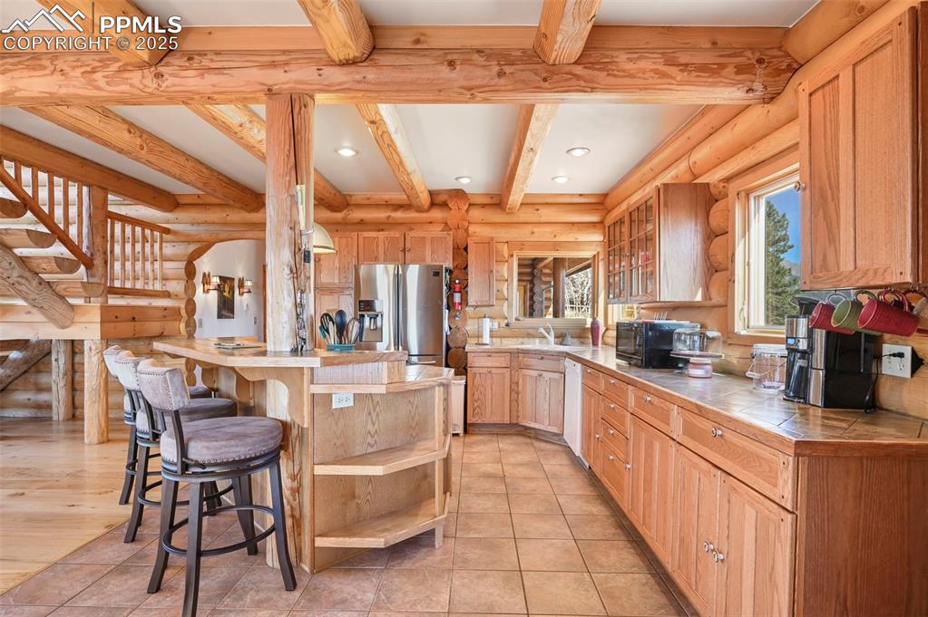 Image 14 of 50: Kitchen with a kitchen bar, tile counters, stainless steel refrigerator wit