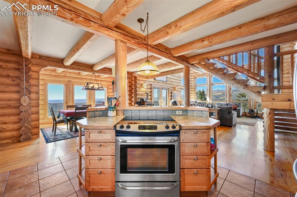 Image 15 of 50: Kitchen with beam ceiling, tile counters, stainless steel range with electr