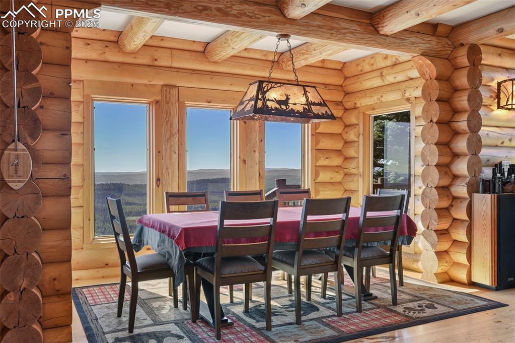 Image 16 of 50: Dining room with log walls, beamed ceiling, a mountain view, and wood finis