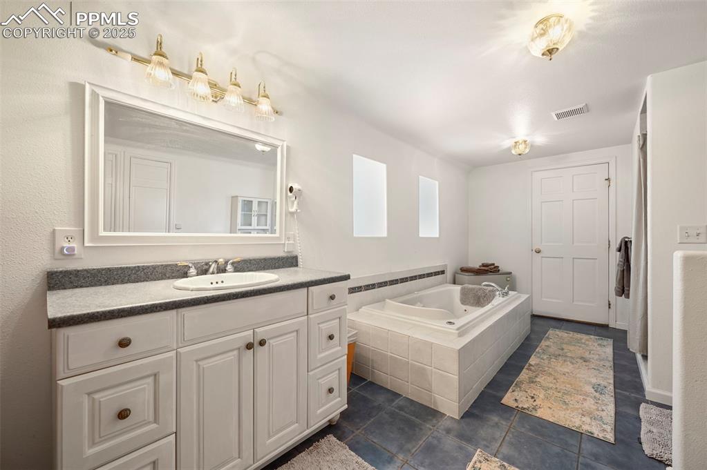 Image 30 of 50: Bathroom with tile patterned floors, vanity, visible vents, and a bath