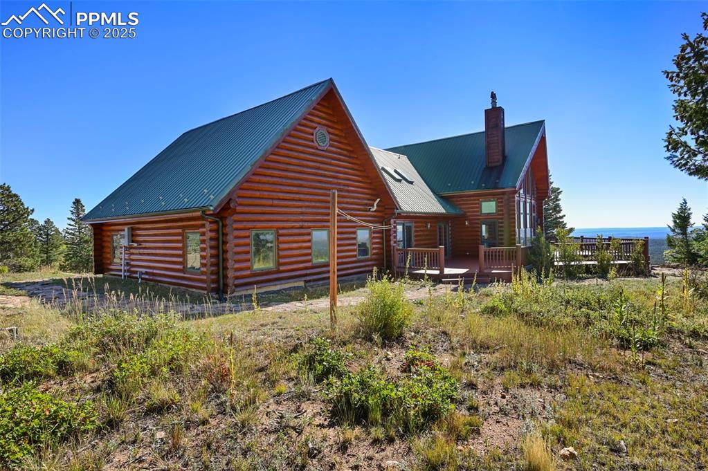 Image 32 of 50: Back of house with a chimney, log siding, a deck, and metal roof