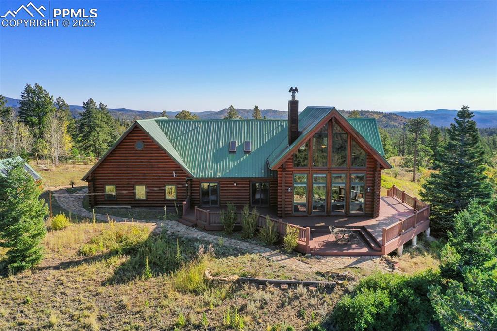 Image 37 of 50: Back of house featuring a deck with mountain view, metal roof, a chimney, a