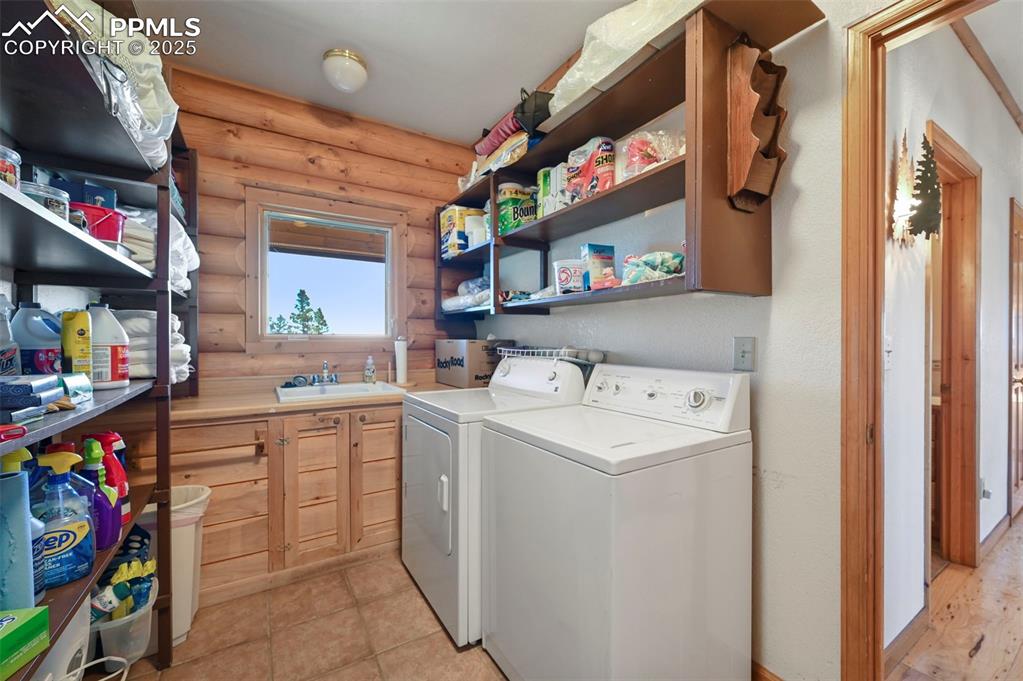 Image 48 of 50: Washroom featuring rustic walls, washer and dryer, cabinet space, and a sin