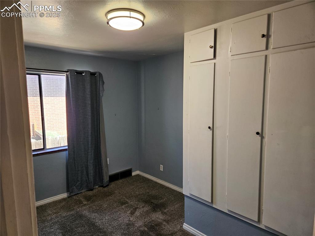 Image 10 of 22: Unfurnished bedroom with dark colored carpet and baseboards