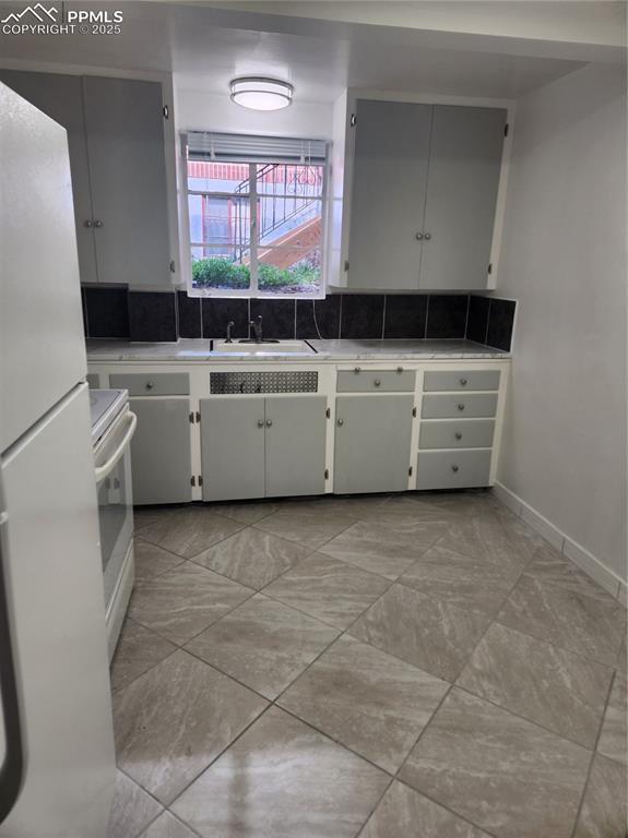 Image 4 of 22: Kitchen featuring refrigerator, a sink, range, light countertops, and baseb