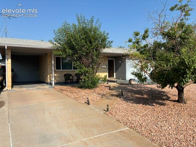 Caption: Brick exterior featuring a covered carport, concrete driveway, and xeriscaped front yard with mature