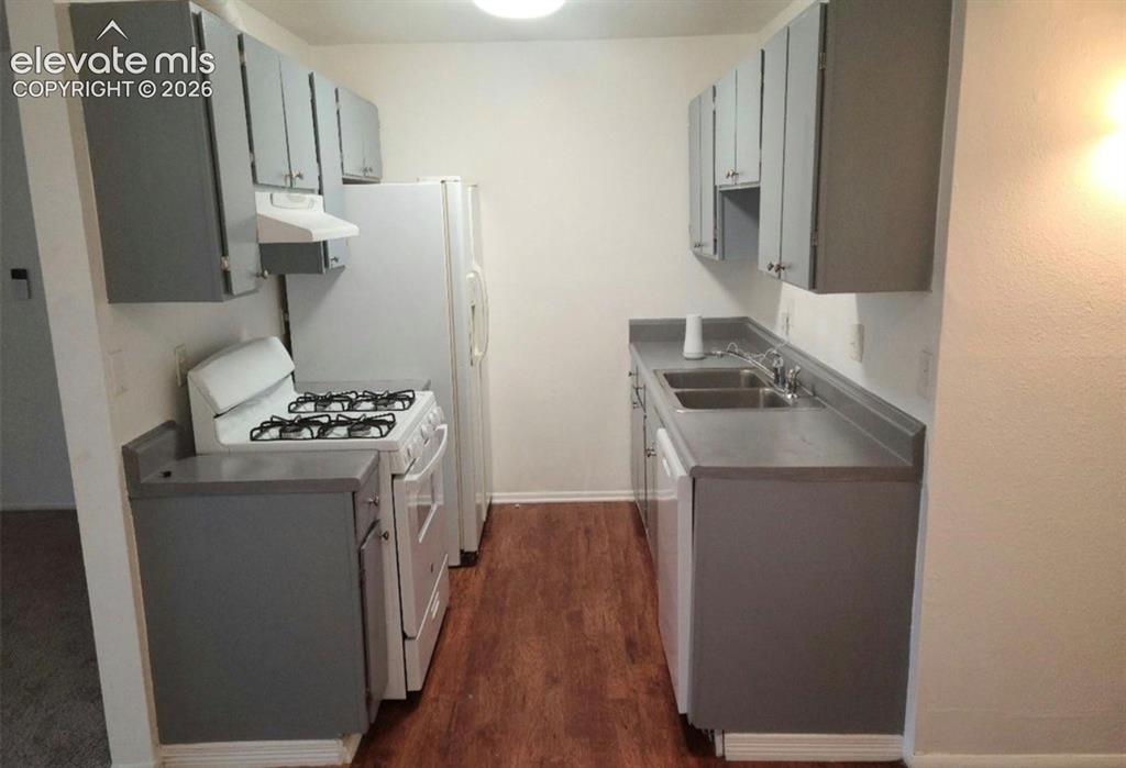 Image 6 of 9: Galley kitchen featuring wood-finish flooring, white walls, and gray cabine