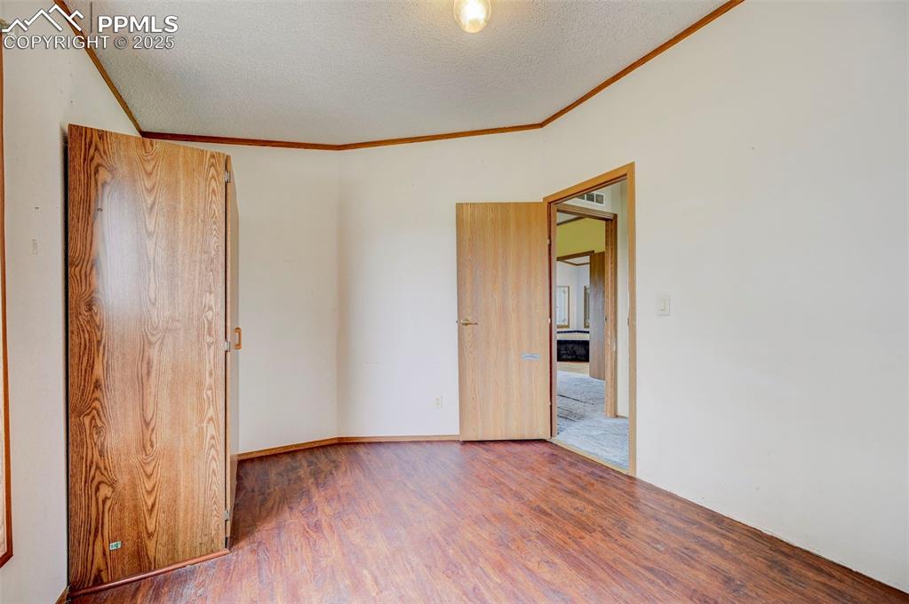 Image 18 of 48: Spare room featuring ornamental molding, wood finished floors, and a textur