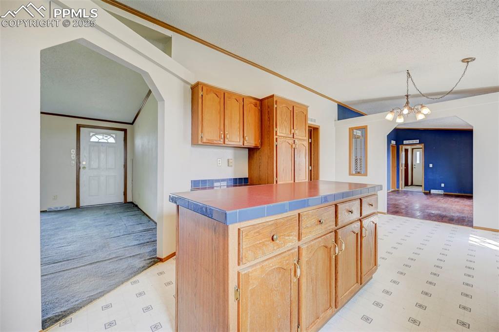 Image 20 of 48: Kitchen featuring a chandelier, a textured ceiling, ornamental molding, bas