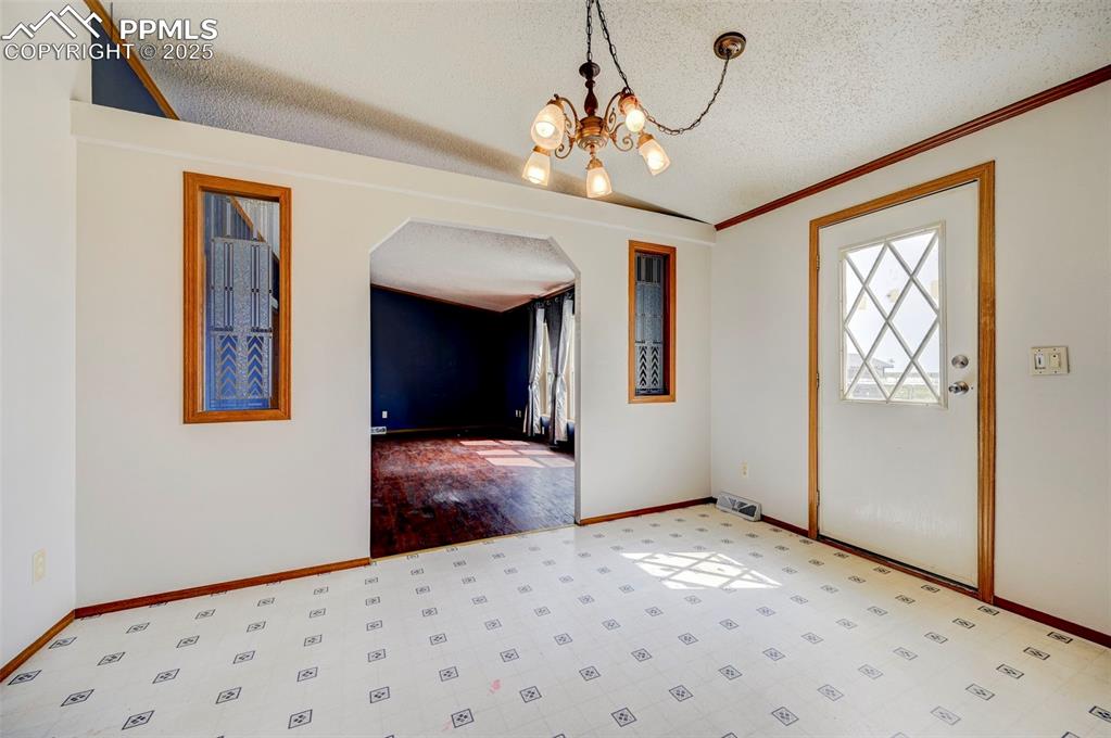 Image 25 of 48: Spare room featuring a textured ceiling, arched walkways, a chandelier, bas