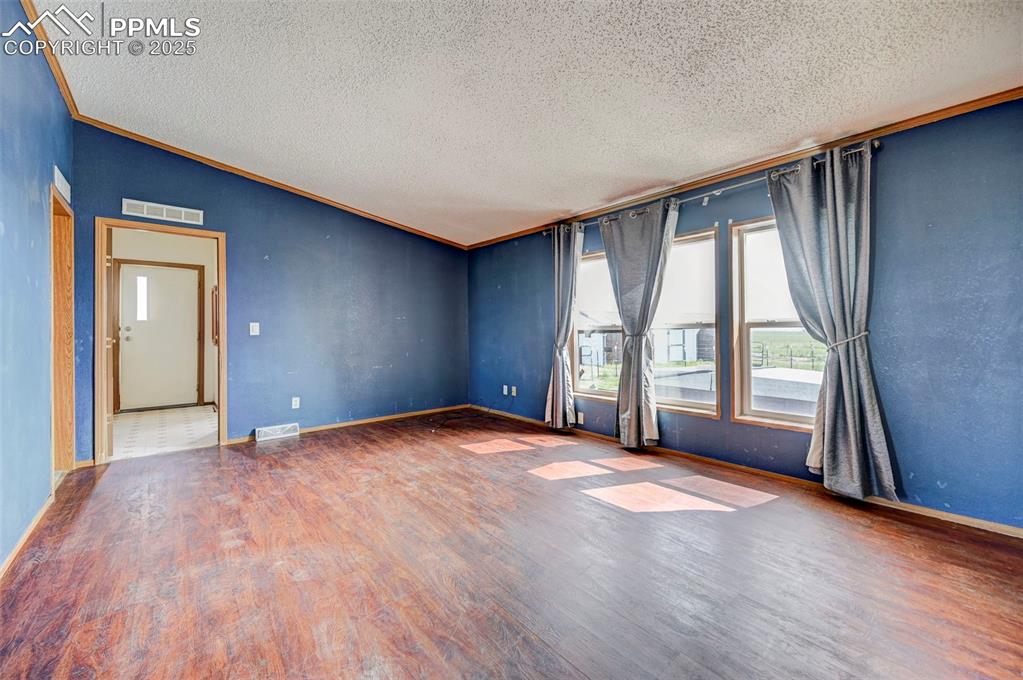 Image 29 of 48: Empty room with a textured ceiling, wood finished floors, crown molding, ba