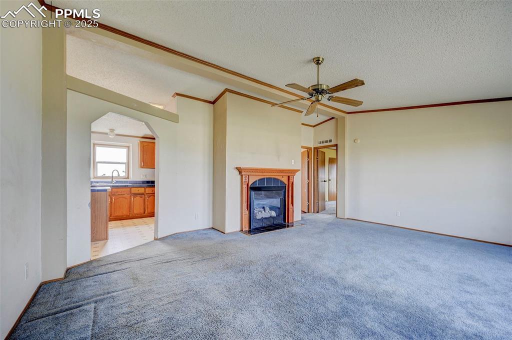 Image 7 of 48: Unfurnished living room featuring a ceiling fan, a textured ceiling, a fire