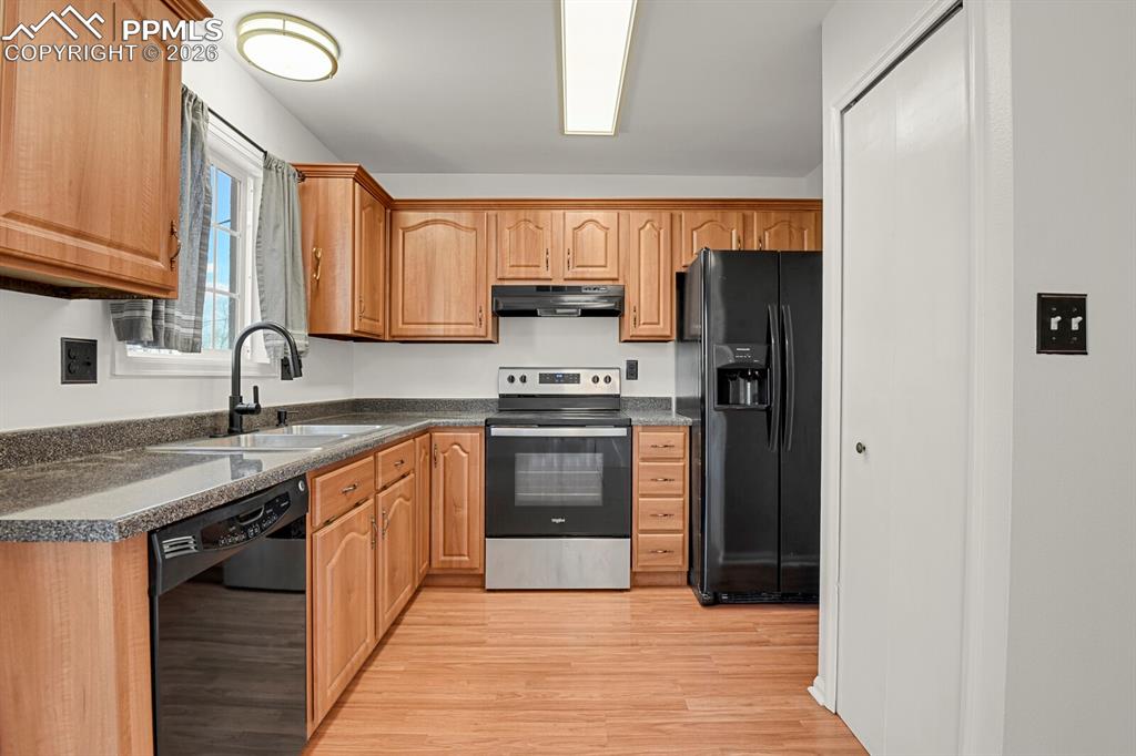 Image 10 of 31: Kitchen with black appliances, light wood-style flooring, and dark stone co