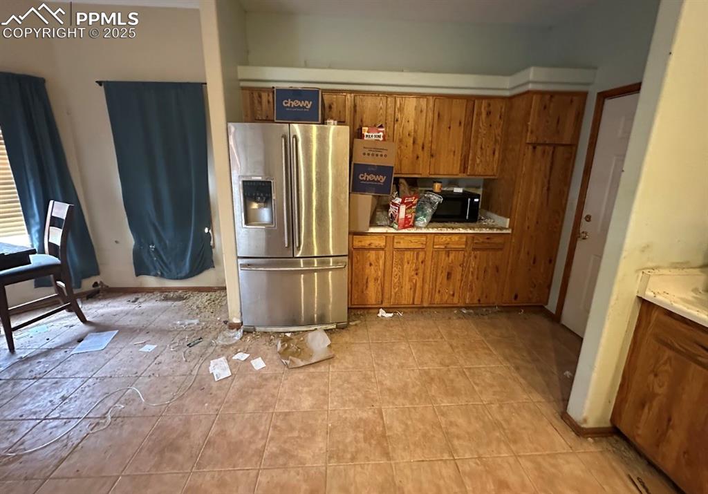Image 13 of 36: Kitchen featuring brown cabinetry, stainless steel refrigerator with ice di