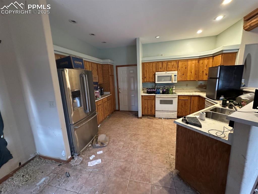 Image 14 of 36: Kitchen featuring brown cabinetry, white appliances, light countertops, and
