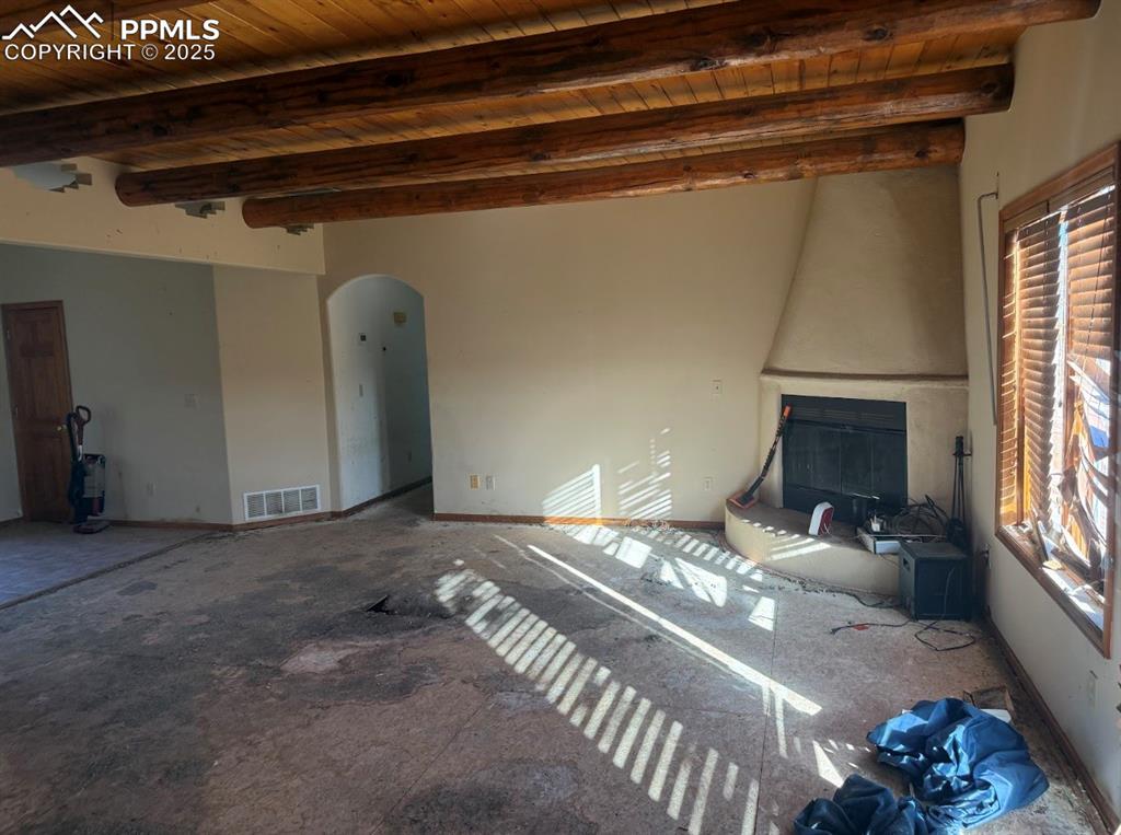 Image 18 of 36: Unfurnished living room with arched walkways and a wooden ceiling with expo