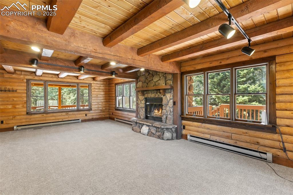 Image 21 of 50: Living area featuring lots of natural light, log walls, a wood-burning ston