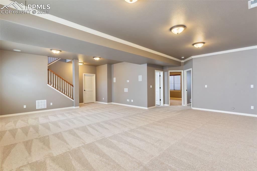 Image 21 of 27: Spare room with stairway, crown molding, and light colored carpet