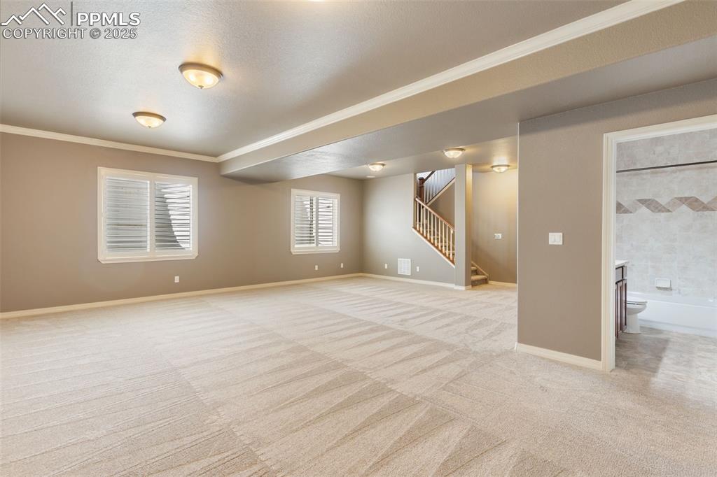 Image 22 of 27: Basement featuring light carpet, ornamental molding, stairs, and a textured