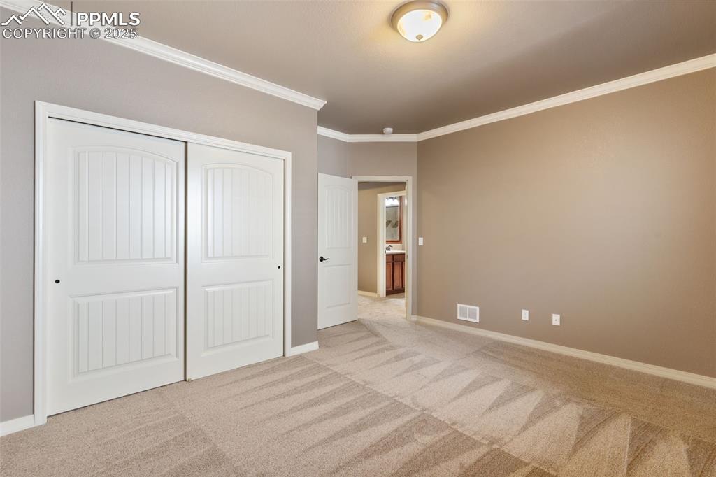 Image 25 of 27: Unfurnished bedroom with crown molding, light colored carpet, and a closet