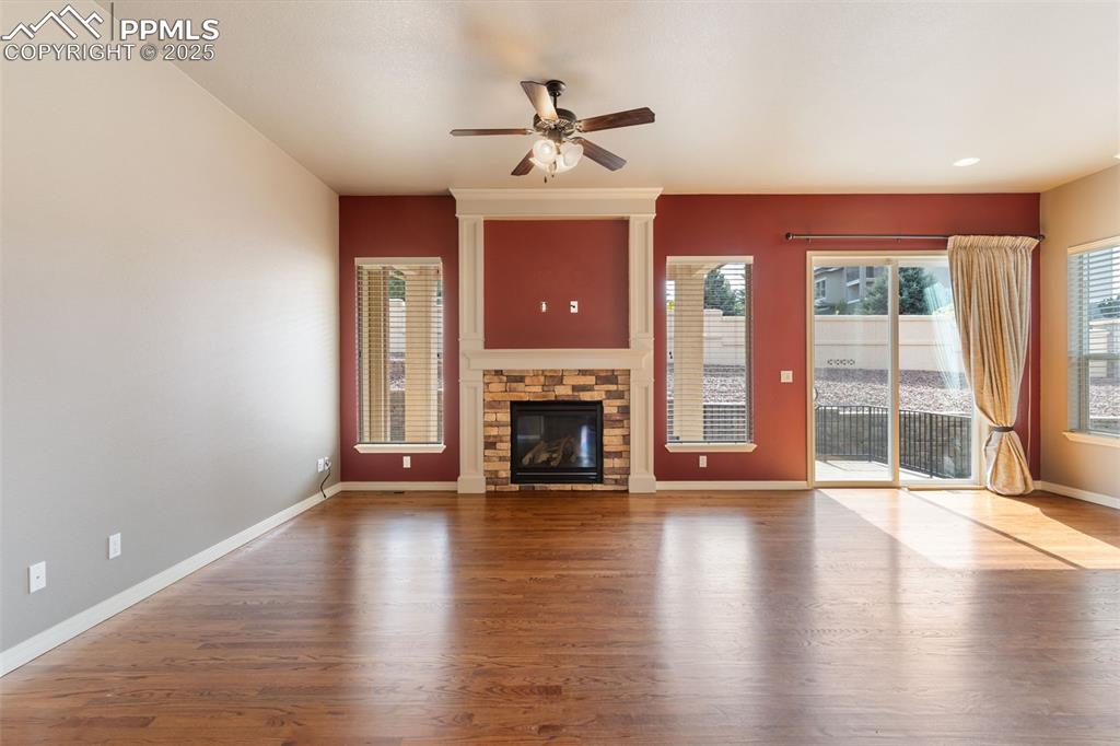 Image 5 of 27: Unfurnished living room with wood finished floors, a stone fireplace, and c