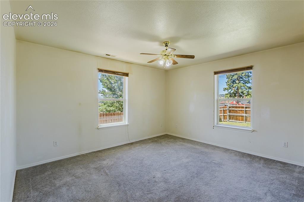 Image 16 of 27: Neutral wall finishes, dual windows, gray carpet, and a ceiling fan with li