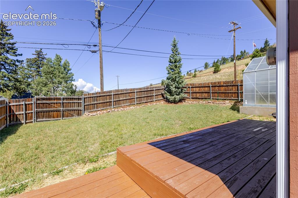 Image 23 of 27: Fenced backyard offers a sunny, ground-level deck, grassy lawn area enclose