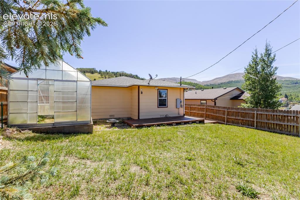 Image 24 of 27: Expansive backyard featuring privacy fencing, a sunny deck, and a greenhous