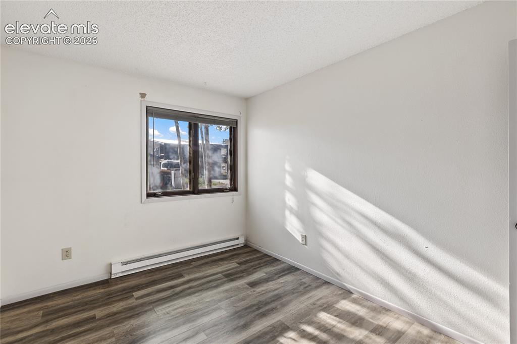 Image 23 of 33: Window with dark trim, baseboard heating unit, and wood-finish flooring