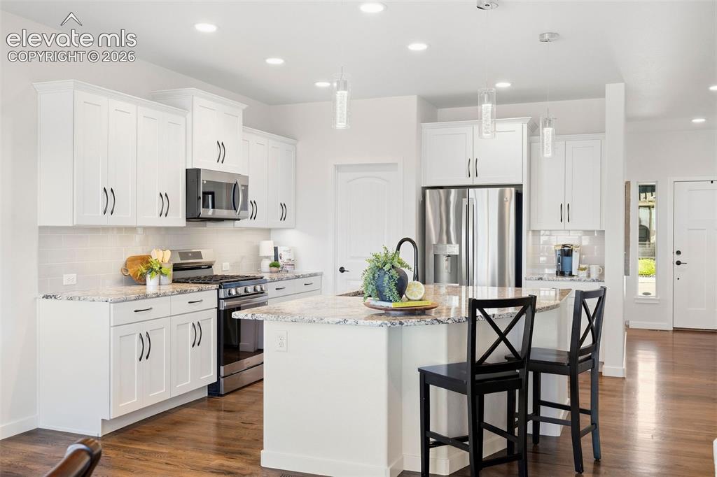 Image 3 of 46: White cabinetry, stainless steel appliances, and island seating anchor the