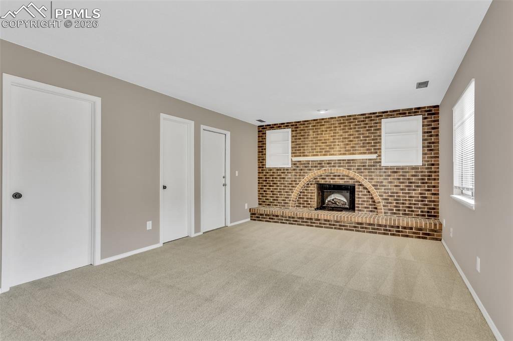 Image 10 of 30: Unfurnished living room with brick wall, a fireplace, light carpet, and an