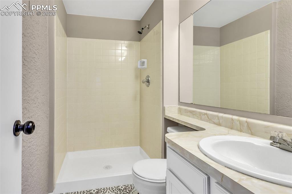 Image 19 of 30: Bathroom featuring a textured wall, vanity, a stall shower, and tile patter