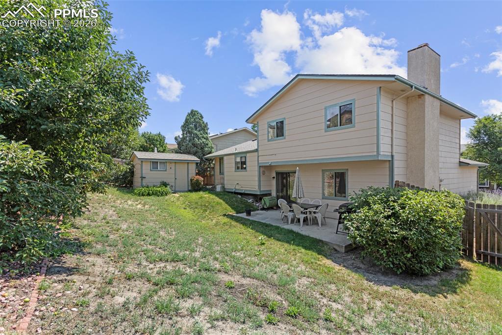 Image 28 of 30: Rear view of house featuring a patio area, a lawn, a chimney, and a shed