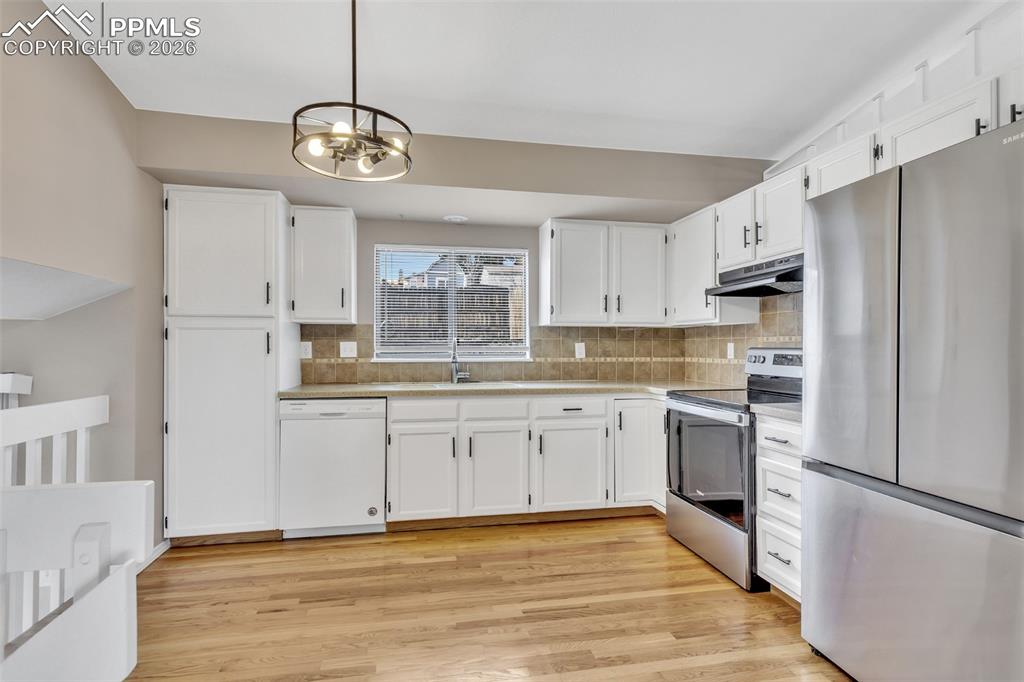 Image 7 of 30: Kitchen with stainless steel appliances, white cabinetry, backsplash, and l